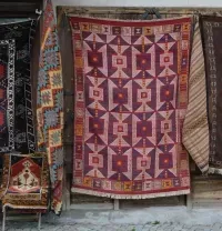 Colorful woven rugs hanging outside a shop, with geometric patterns in red, brown, and black.