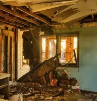 Damaged room with exposed beams, broken walls, and debris scattered across the floor