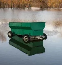 Green floating hopper on calm water with a reflection, near a wooded shoreline