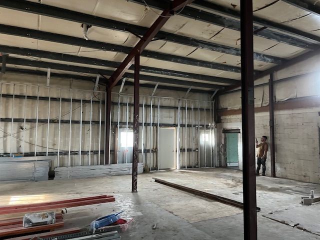 Interior of a warehouse with exposed metal beams and studs, some daylight coming in.