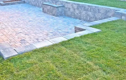 Stone patio beside green lawn with raised retaining wall and steps