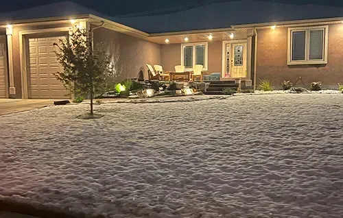 Snow-covered house exterior at night with warm porch lights and a lit front entry.