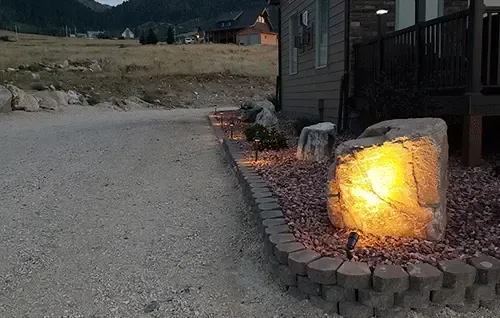 Glowing outdoor rock garden light beside a house at dusk