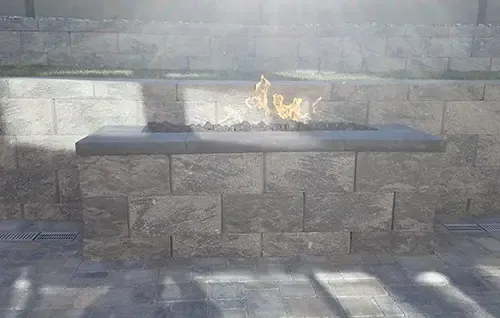 Stone outdoor wall with a narrow ledge and a small flame burning in the center