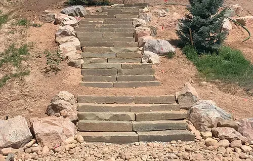 Stone steps climbing a dry hillside, bordered by rocks and sparse greenery