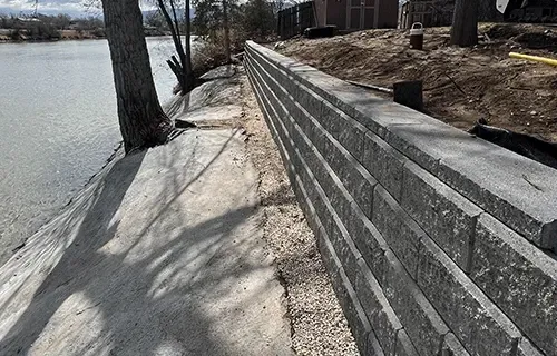 Stone retaining wall along a lakeside path with trees and water on the left