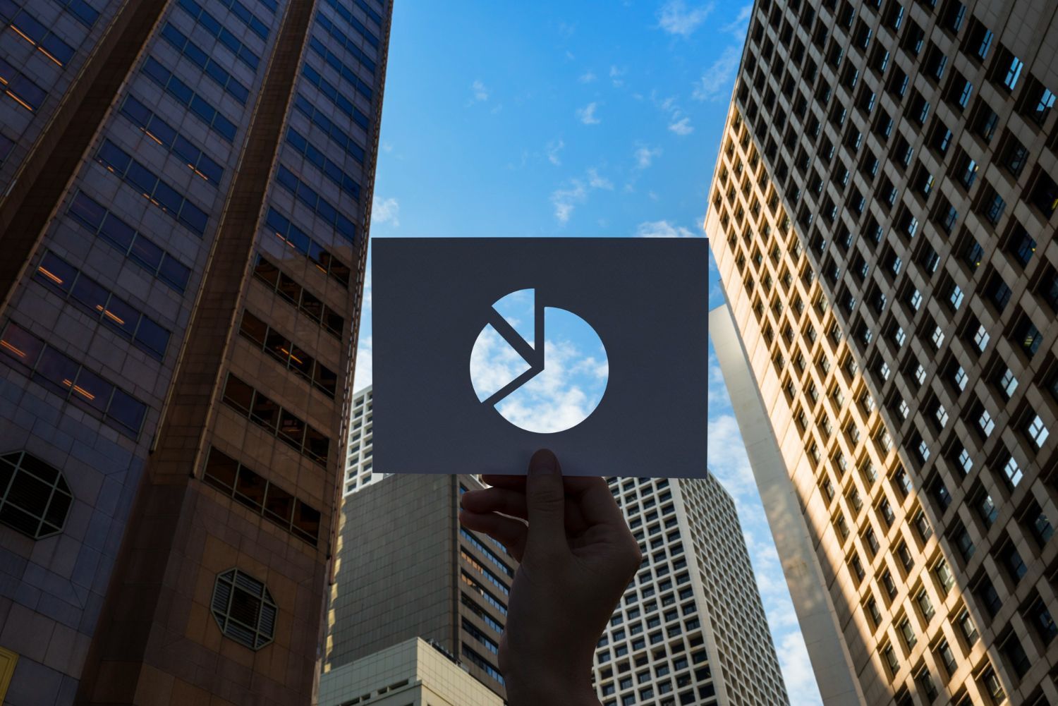 Person holding pie chart cutout against cityscape.