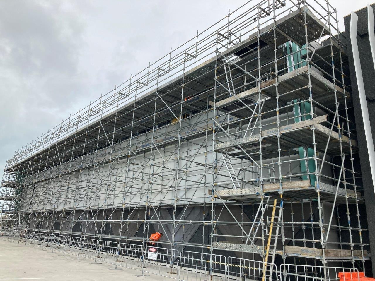 Scaffolding surrounds a large building under construction, with workers and ladders visible.