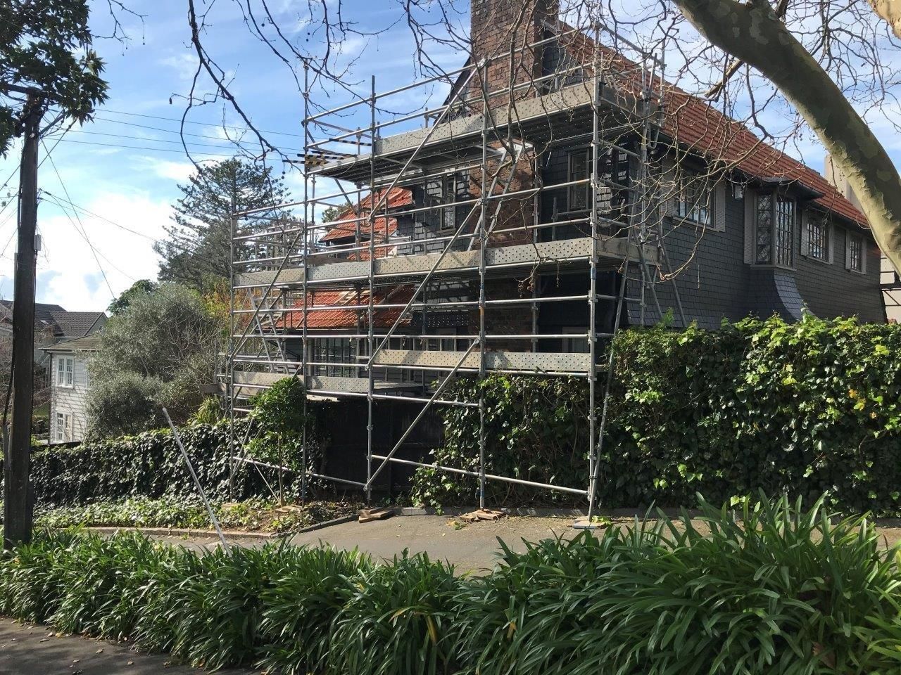 House under renovation with scaffolding, surrounded by greenery and trees in daylight