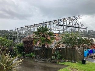 Partly built metal greenhouse frame in a muddy garden with wooden fencing and overcast sky