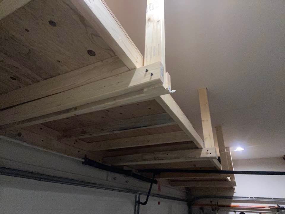 Wooden storage shelves installed in a garage, attached to the ceiling and walls.