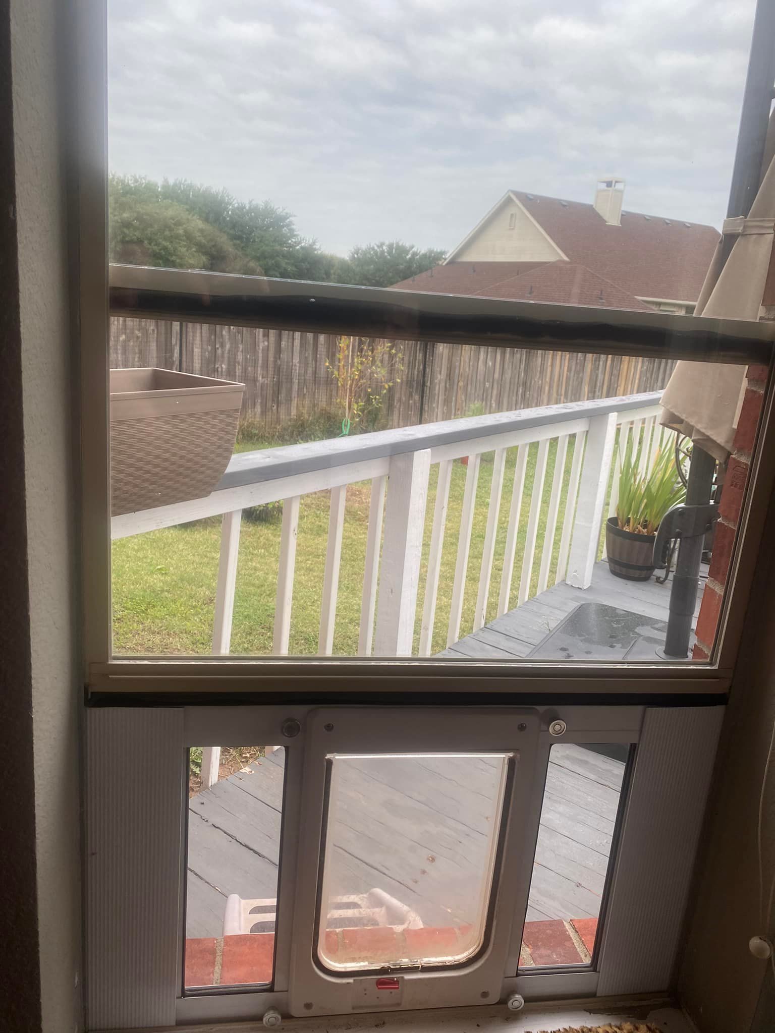 Window with built-in pet door. Backyard view includes deck, lawn, fence, and cloudy sky.
