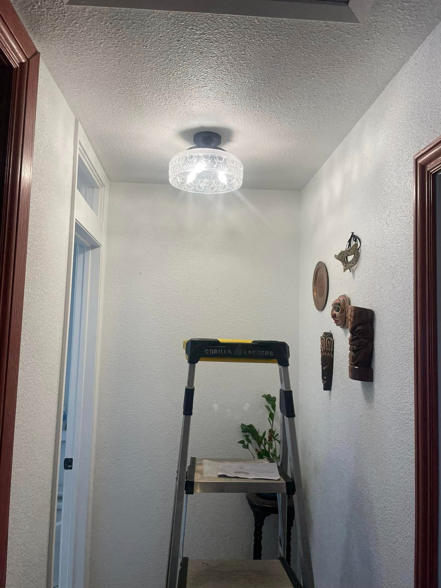 Hallway with textured walls, a ceiling light, and a stepladder. Decorative items on the right wall.