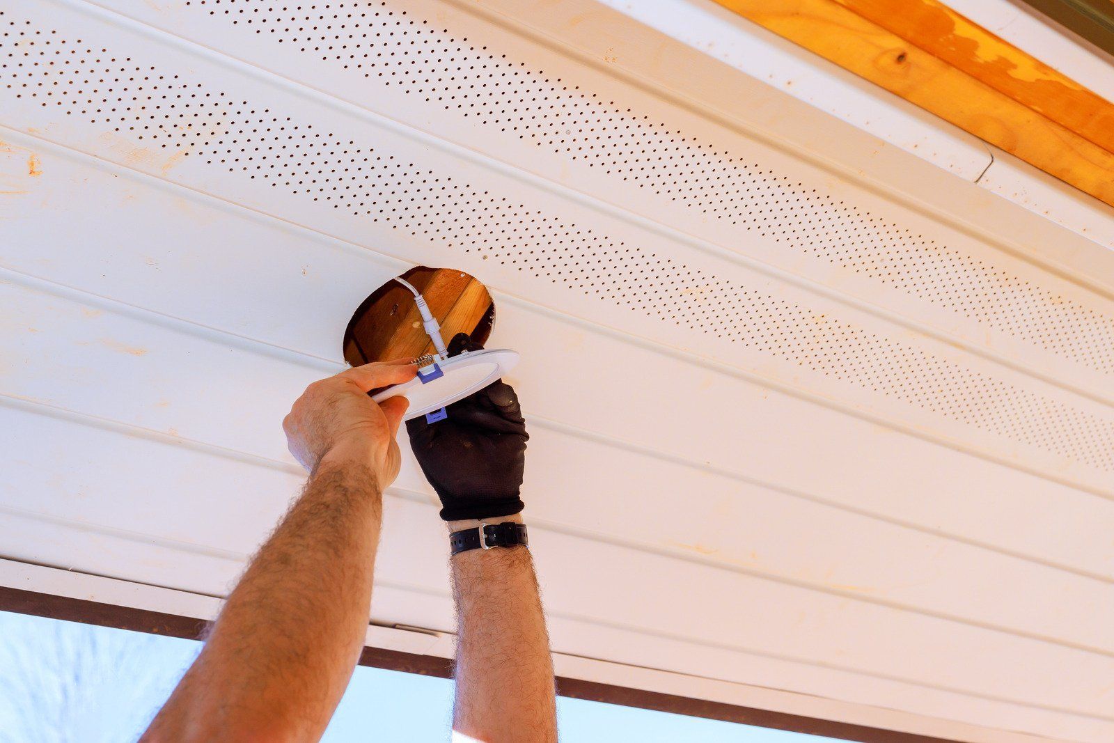 Person applying caulk to a hole in white perforated soffit.