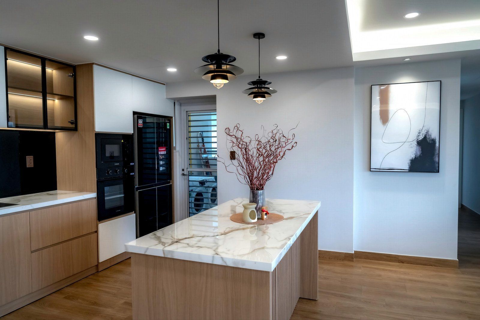 Modern kitchen with marble island, wooden cabinets, and decorative pendant lights.