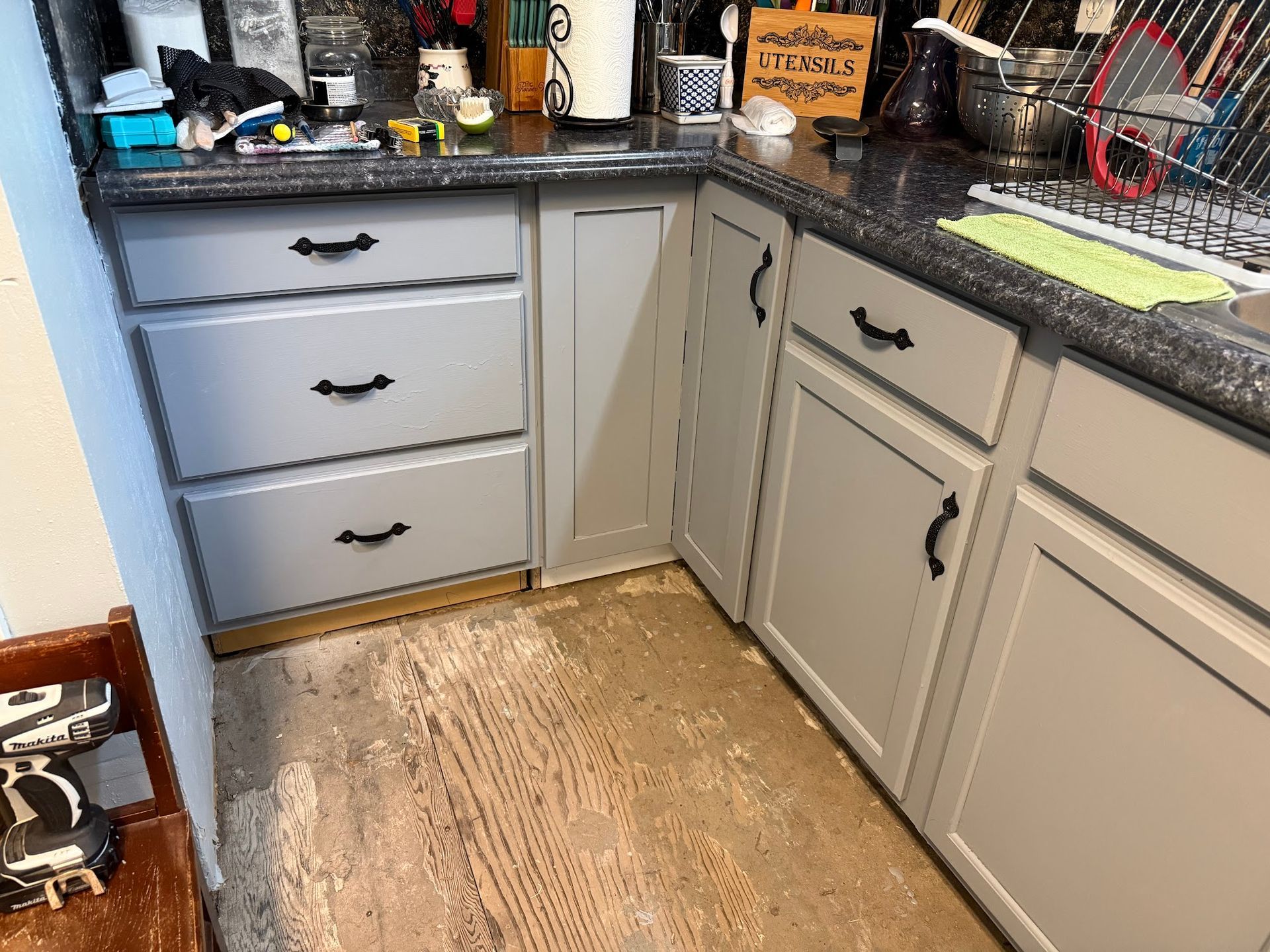 Kitchen cabinets with gray paint and black hardware, set over a light-colored wooden floor.