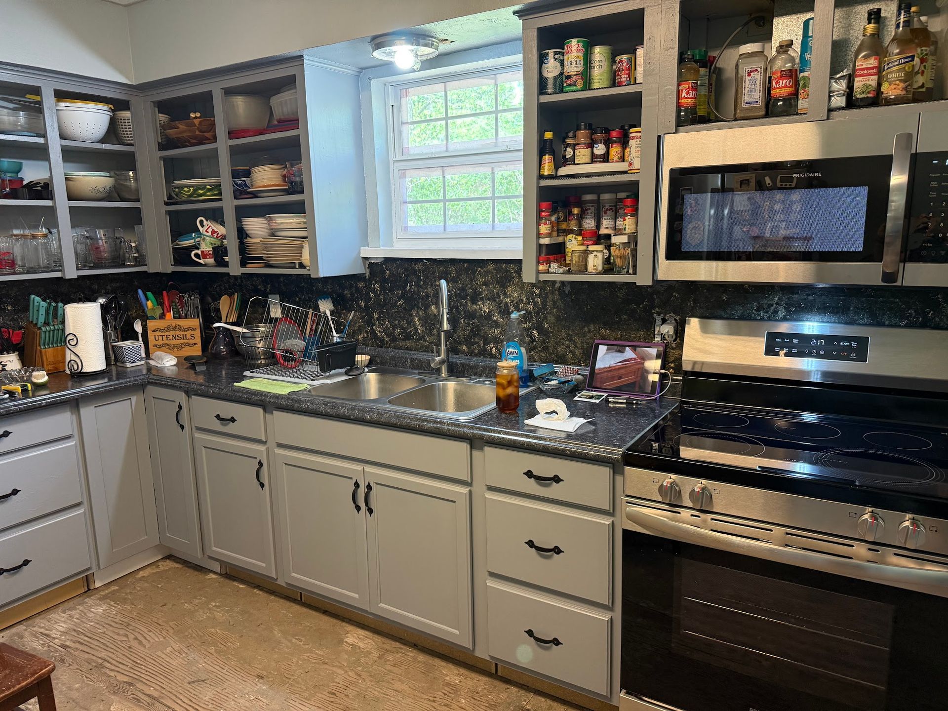 Kitchen with gray cabinets, black countertops, stainless steel appliances, and a window.