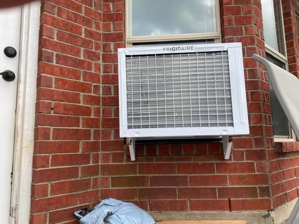 White Frigidaire air conditioner unit mounted on a red brick exterior wall beneath a window.