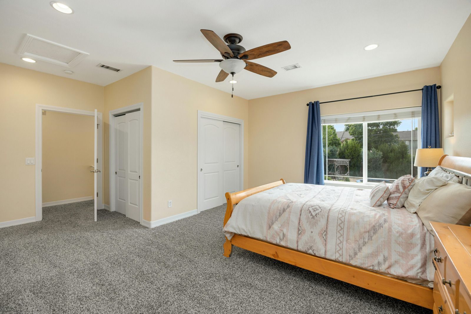 Bedroom with bed, closet, and window, neutral tones, with blue curtains and carpet.