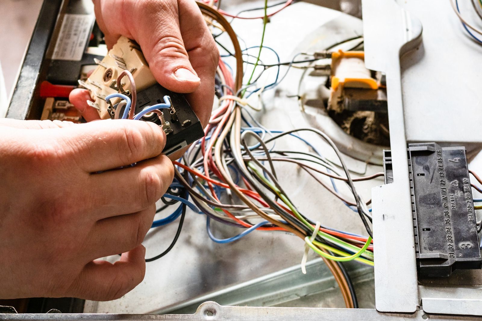 Person's hands working on tangled electrical wires inside a metal appliance.