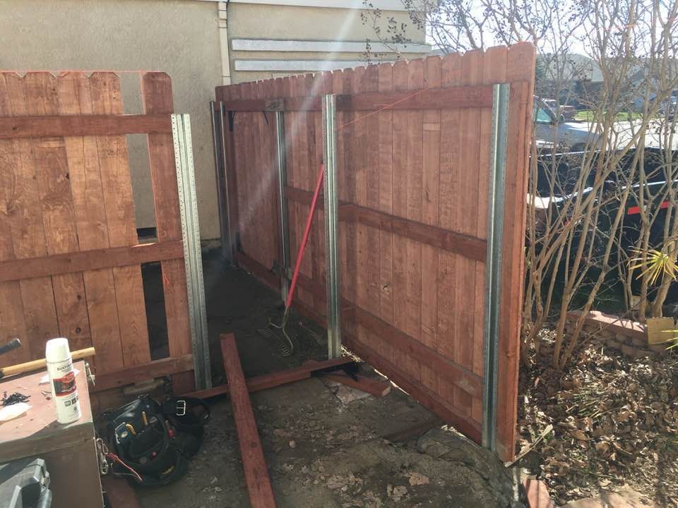 A partially built wooden fence with metal support beams outdoors.