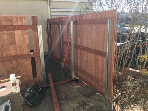 Wooden fence sections in progress, metal posts installed. Construction outdoors, daylight.