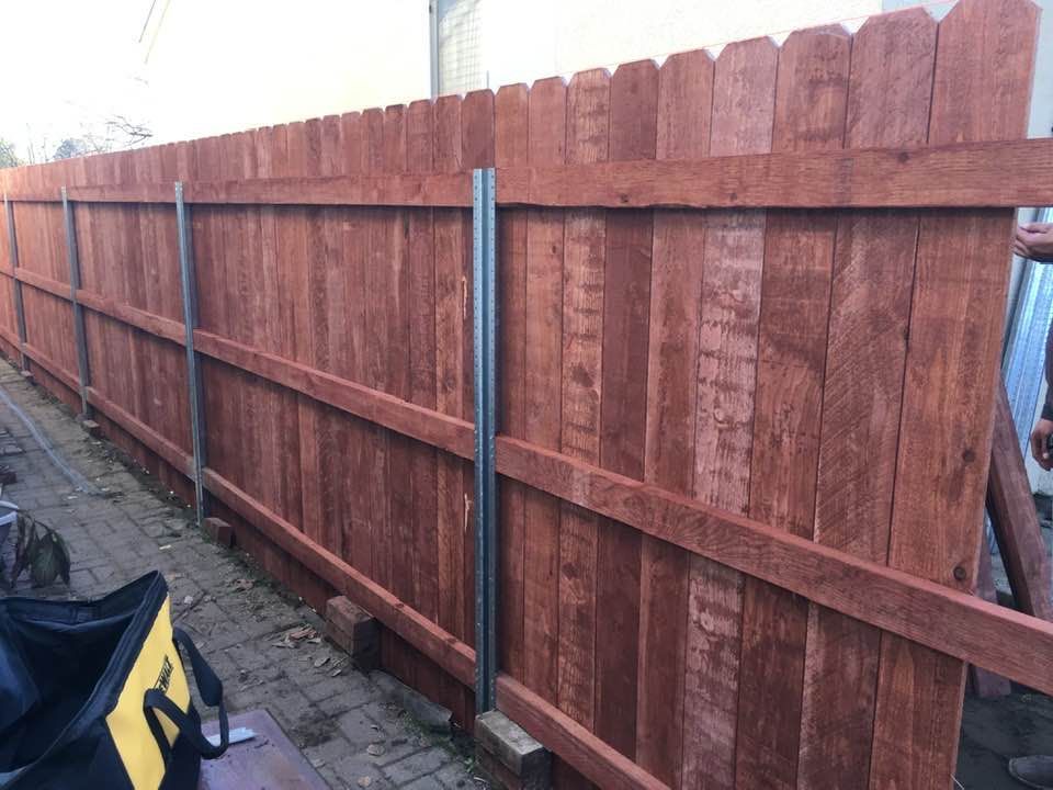 Red wooden fence with vertical metal support posts along a paved area.