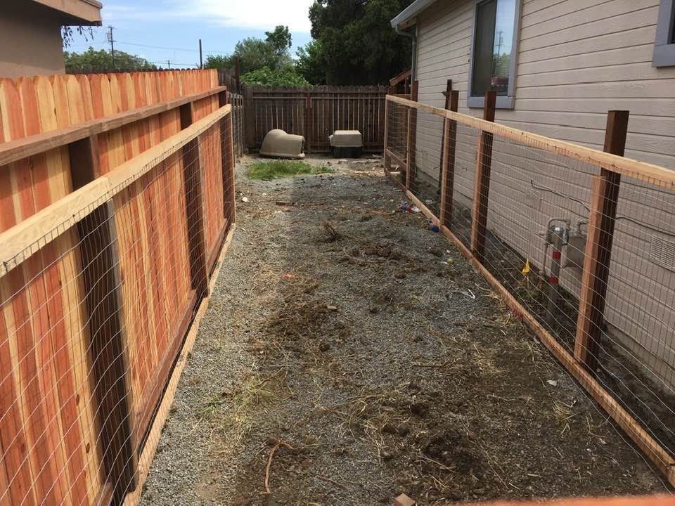 Narrow backyard path with gravel and fences on either side.