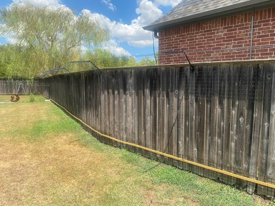 Wooden backyard fence with weathered appearance, next to a grassy lawn and brick house.