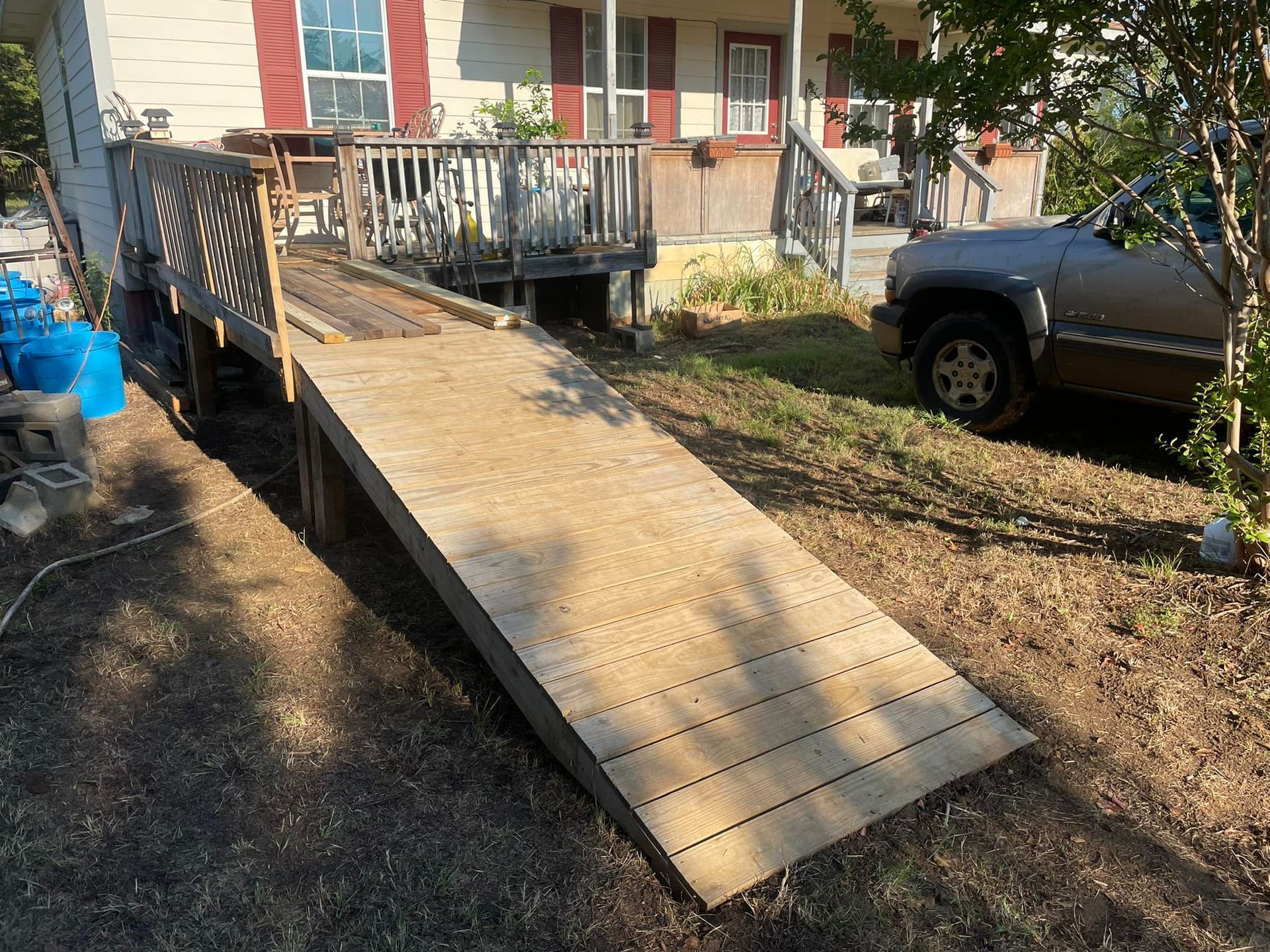 Wooden wheelchair ramp leading to a house entrance. A vehicle is parked in the yard beside it.