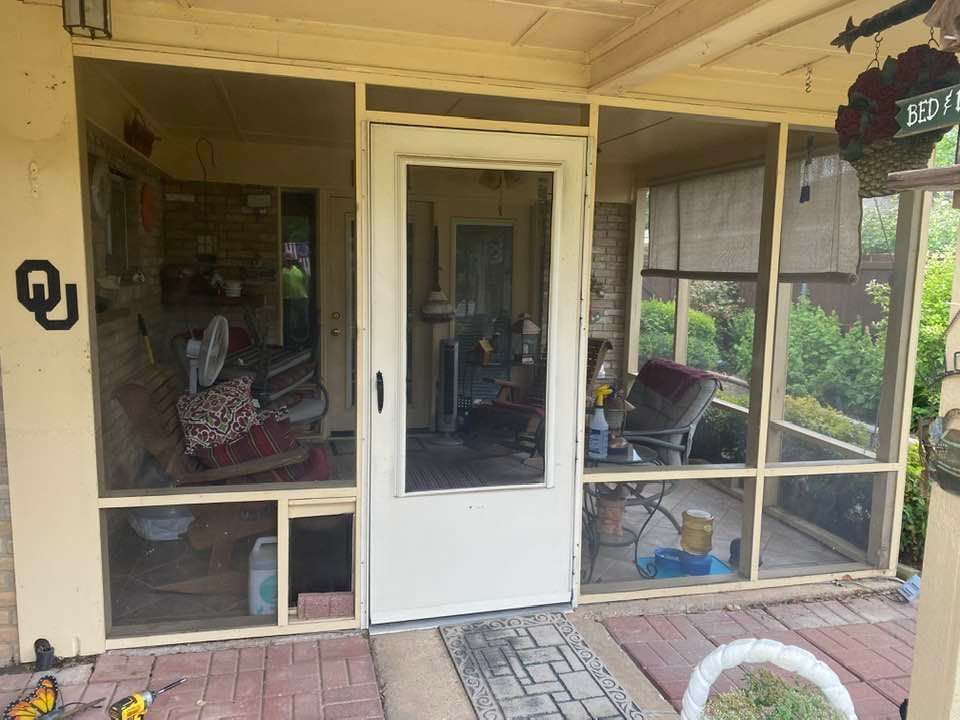Screened-in porch with a white door. Beige frame, brick floor, chairs, and fan visible.
