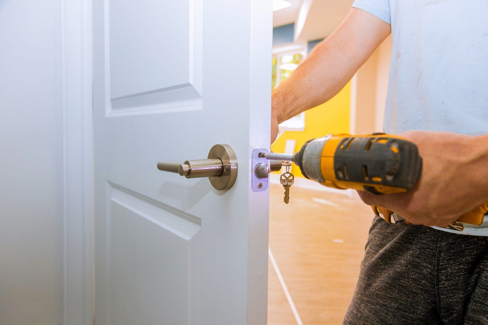 Person using a drill to install a door lock on a white door.