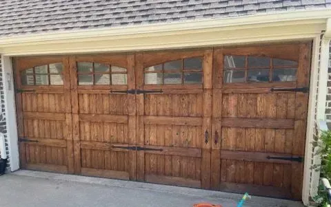 Wooden garage door with arched windows and black hardware.