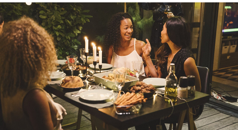 A group of women are sitting at a table with plates of food and candles.