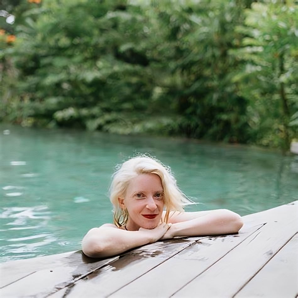 a woman is leaning on a wooden deck in a swimming pool .