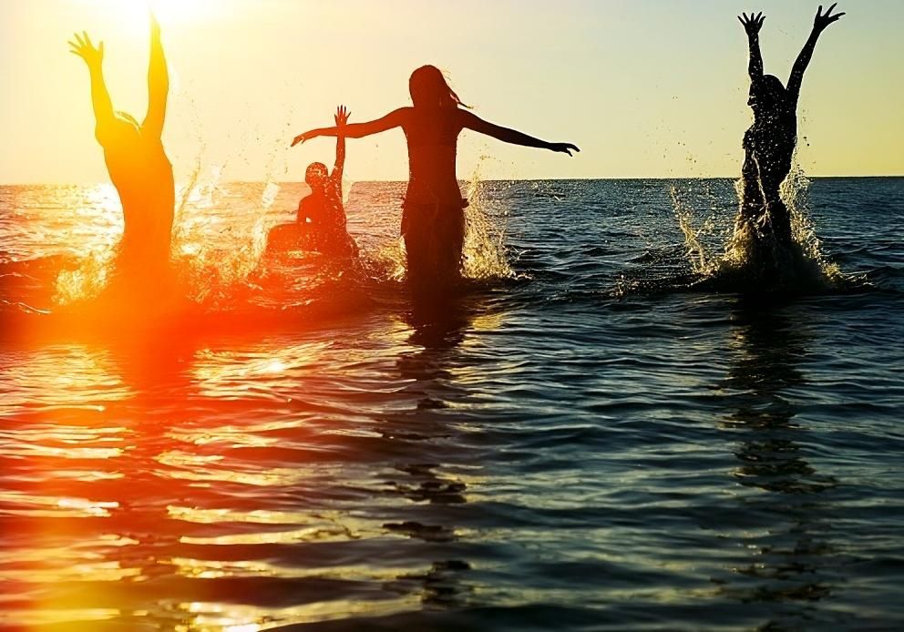 a group of people are jumping into the ocean at sunset .