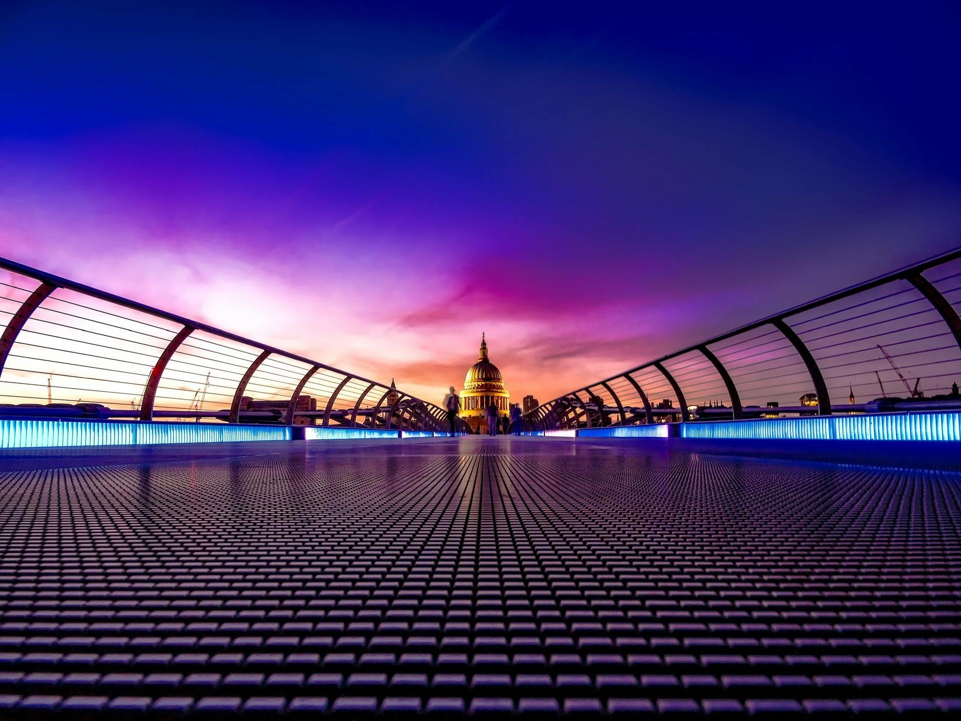 London's Millennium Bridge at sunset, leading to St. Paul's Cathedral. Purple and blue sky.