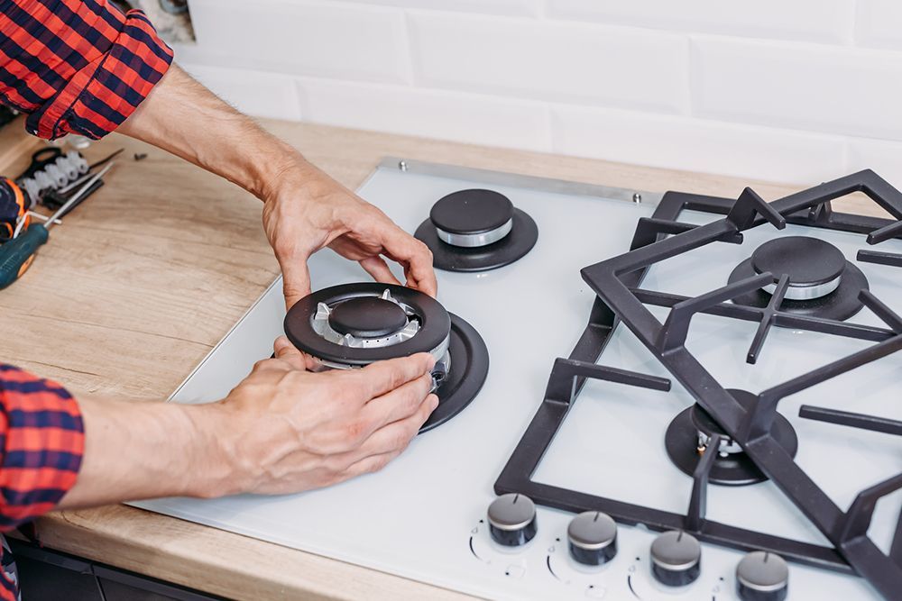 A man is fixing a gas stove in a kitchen.
