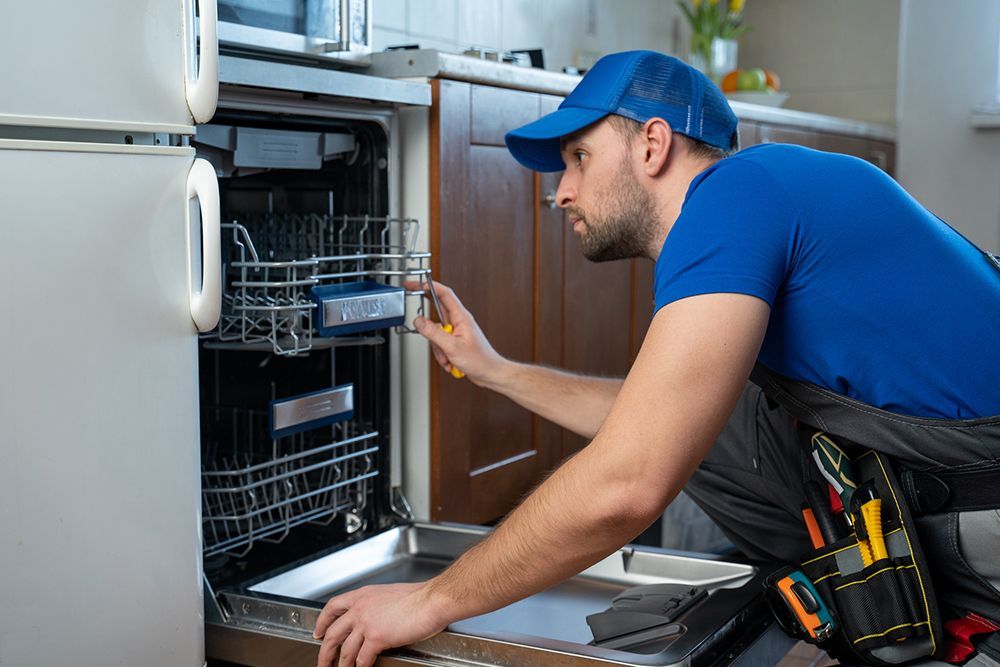 A man is fixing a dishwasher in a kitchen.