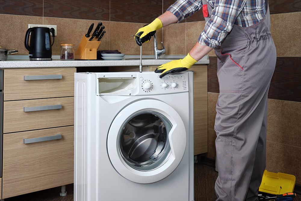A man is fixing a washing machine in a kitchen.
