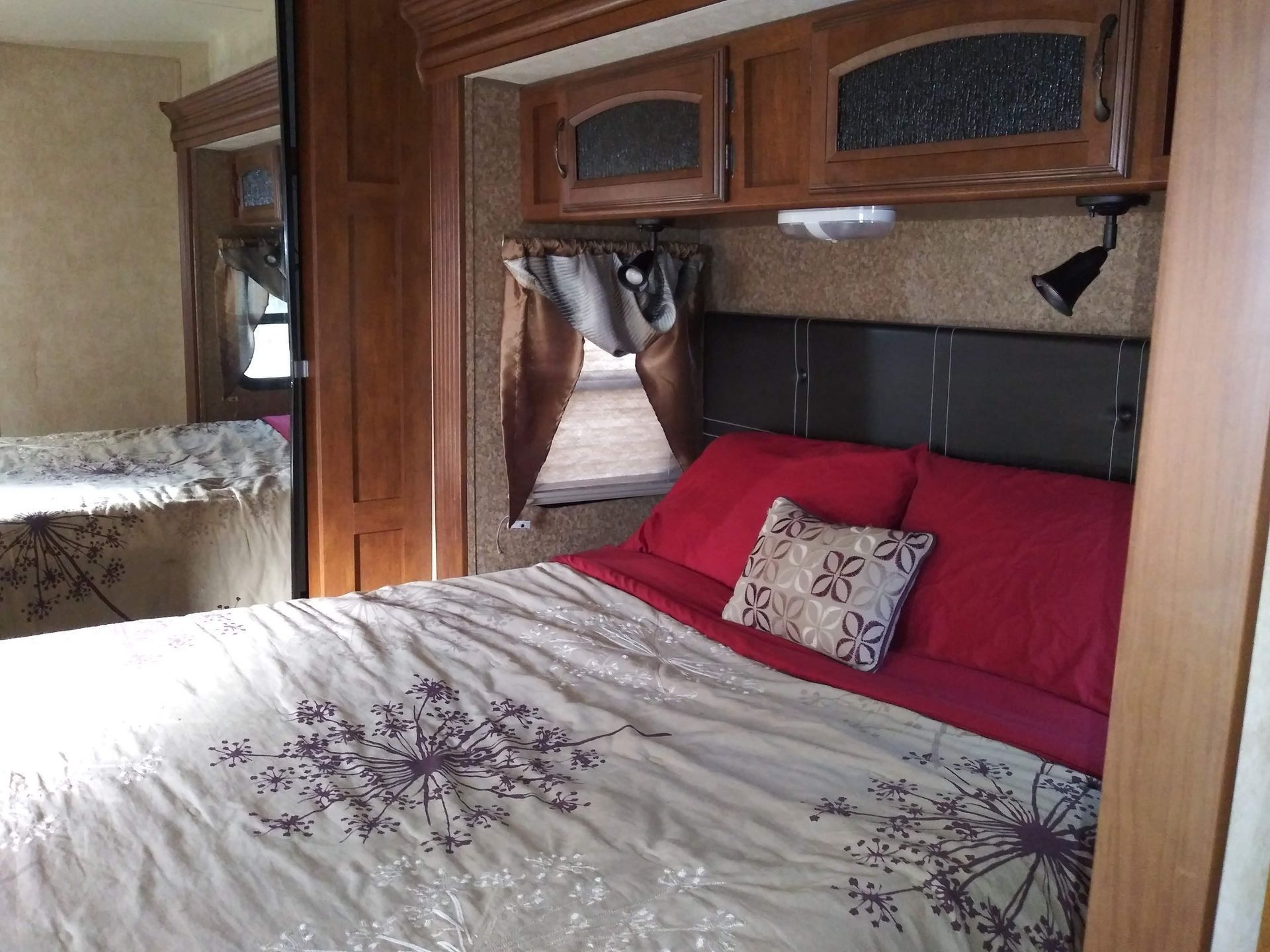 Cozy RV bedroom with a bed, pink pillows, floral comforter, and wooden cabinets