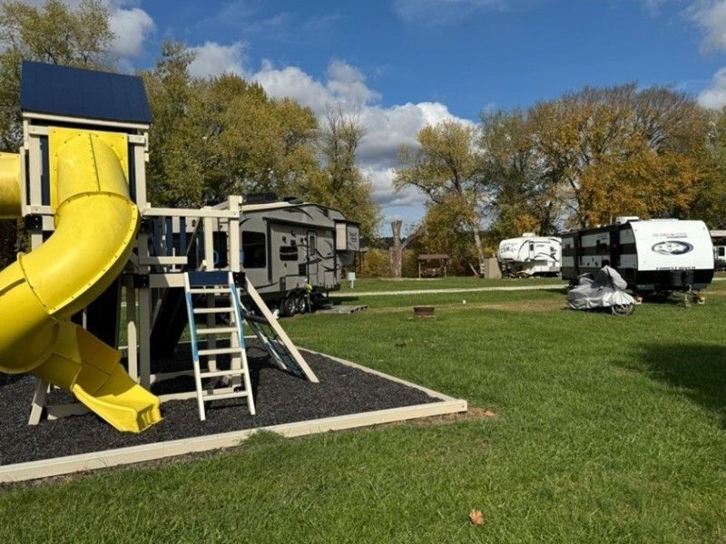 Yellow playground slide beside RV trailers in a grassy campground under a blue sky