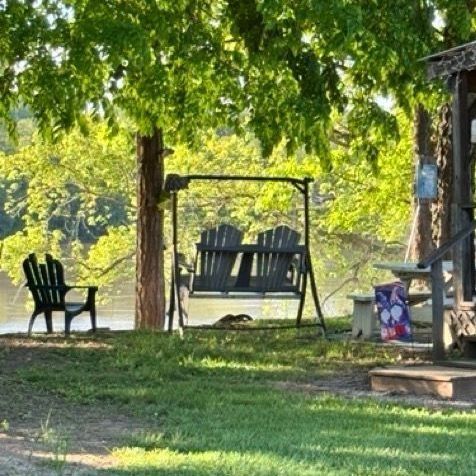 Shaded backyard with two black chairs, a hanging swing bench, and a wooden deck under leafy trees