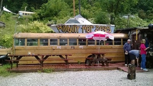Wooden hot dog stand in a wooded area with people ordering at the counter