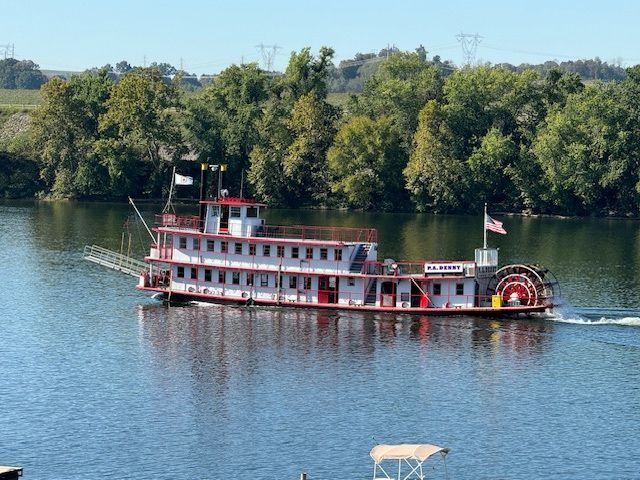 Red and white riverboat cruising on a calm blue river with trees along the far bank.
