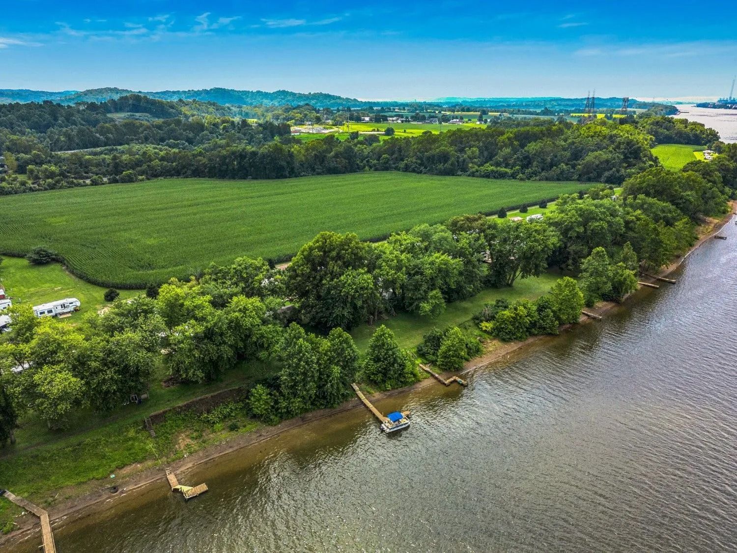 Aerial view of green farmland beside a river under a blue sky
