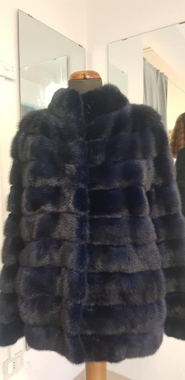 Una pelliccia blu scuro a pannelli orizzontali esposta su un manichino davanti a una parete bianca con specchi.