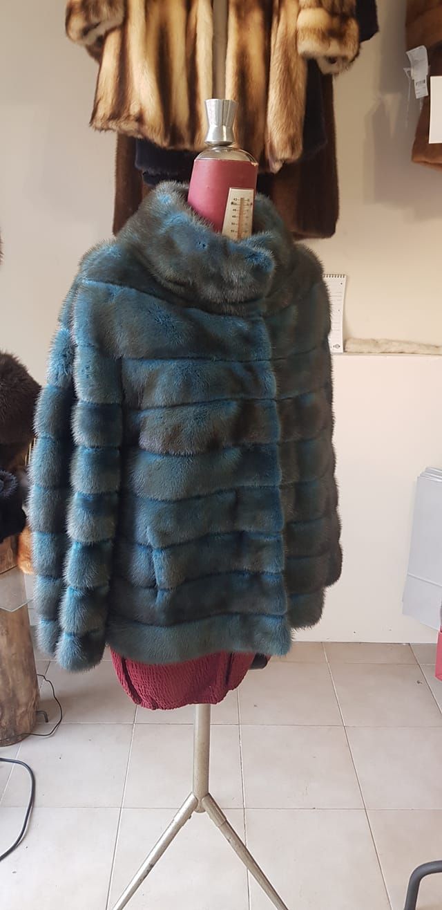 In un negozio, un manichino indossa una giacca di pelliccia a pannelli orizzontali color blu petrolio