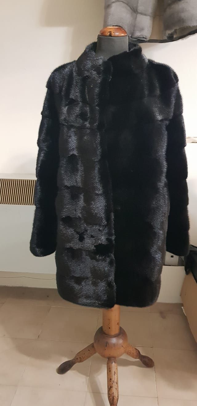 Un cappotto di pelliccia nera e dalla texture particolare, esposto su un manichino di legno in una stanza.
