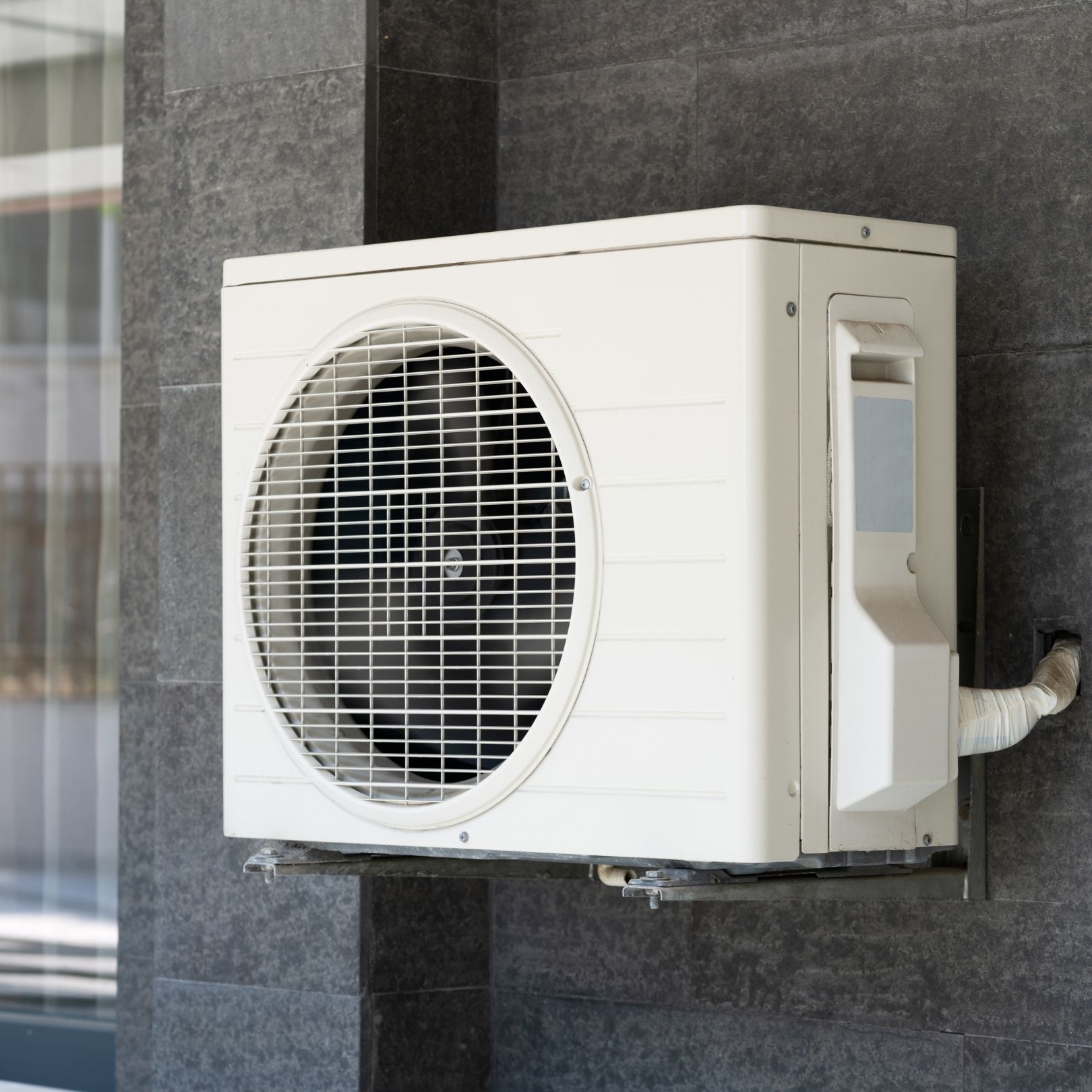 Wall-mounted outdoor air conditioner unit on a dark stone exterior wall